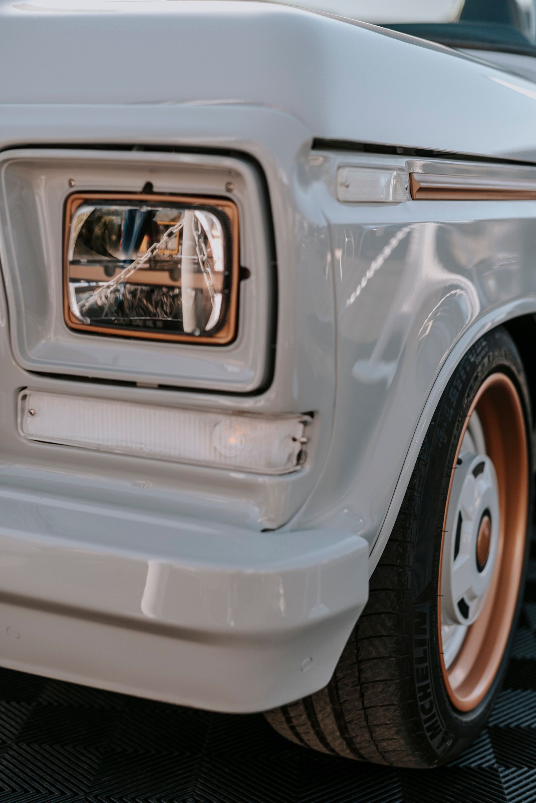 Close-up of a classic white truck's headlight and wheel, highlighting vintage design.