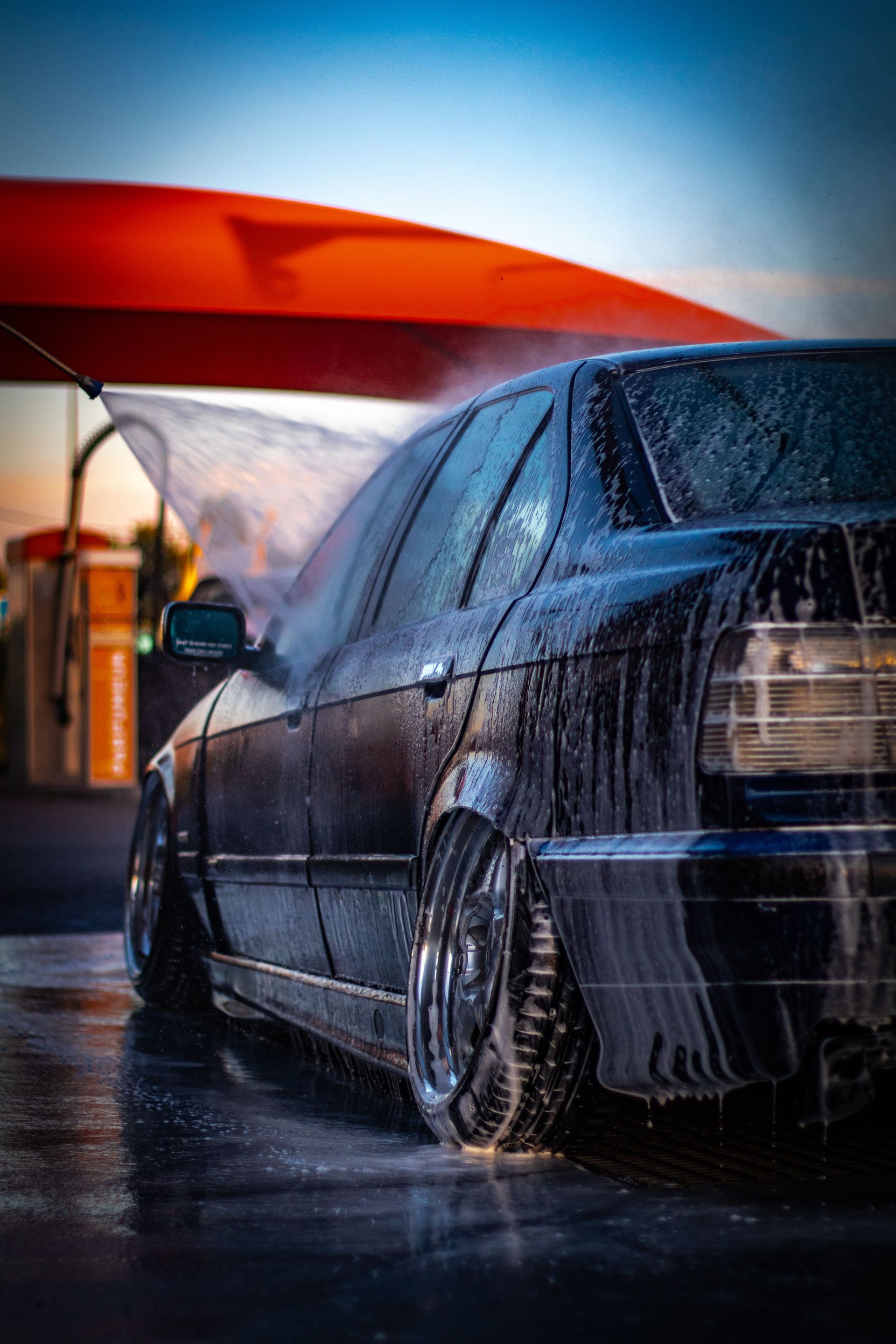 A car wash in progress with soap and water on a car under a vibrant sky.