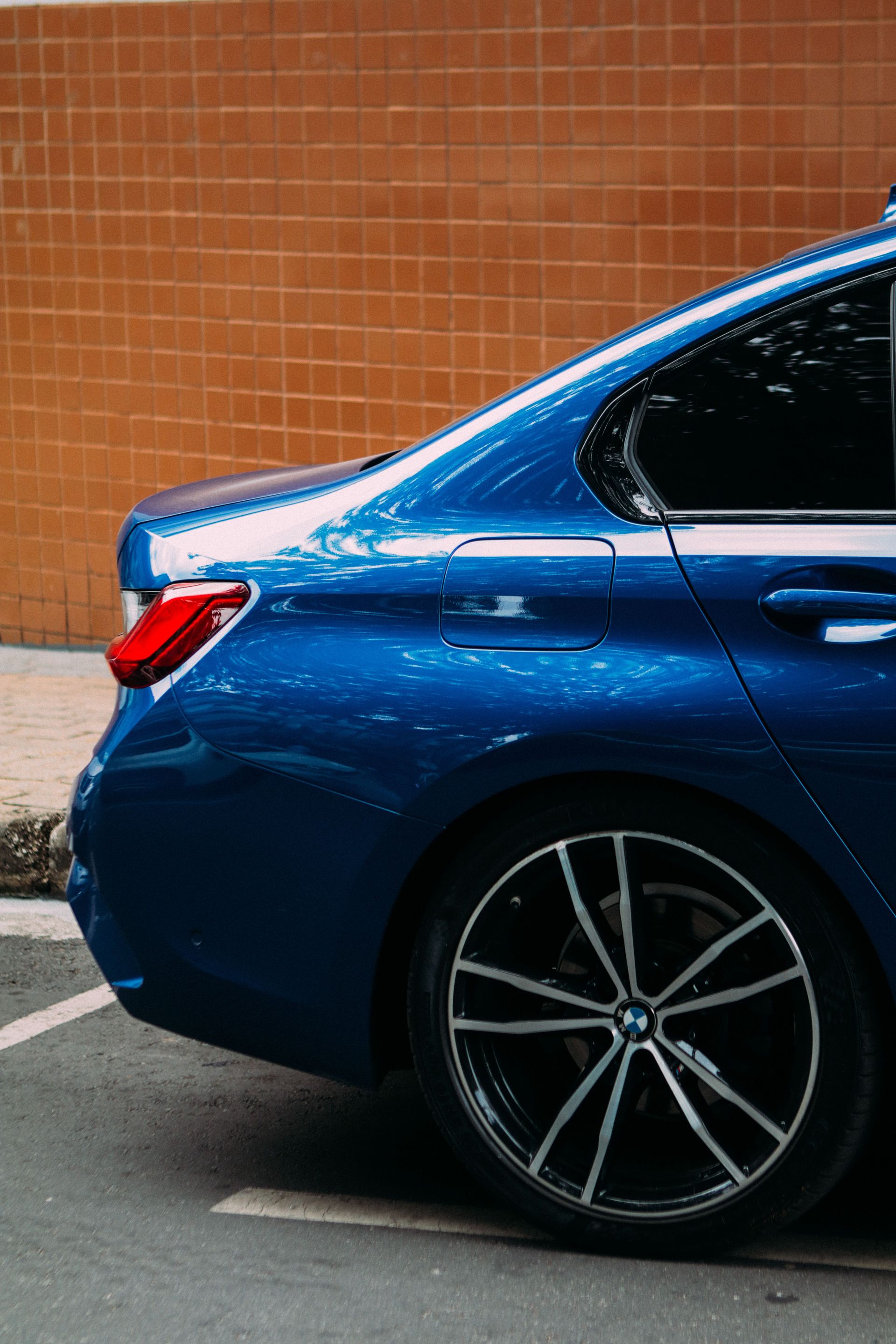 A sleek blue car with alloy wheels parked in a city area with an orange wall.